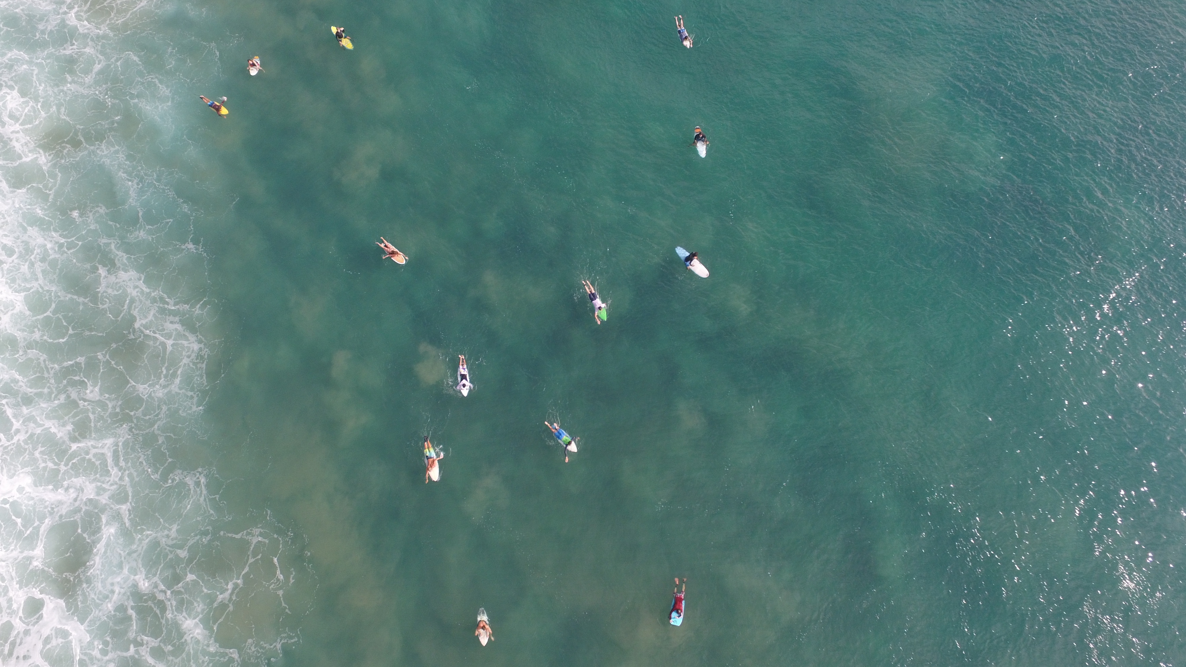 Top-down aerial of surfers waiting in the lineup in clear water at Arugam Bay