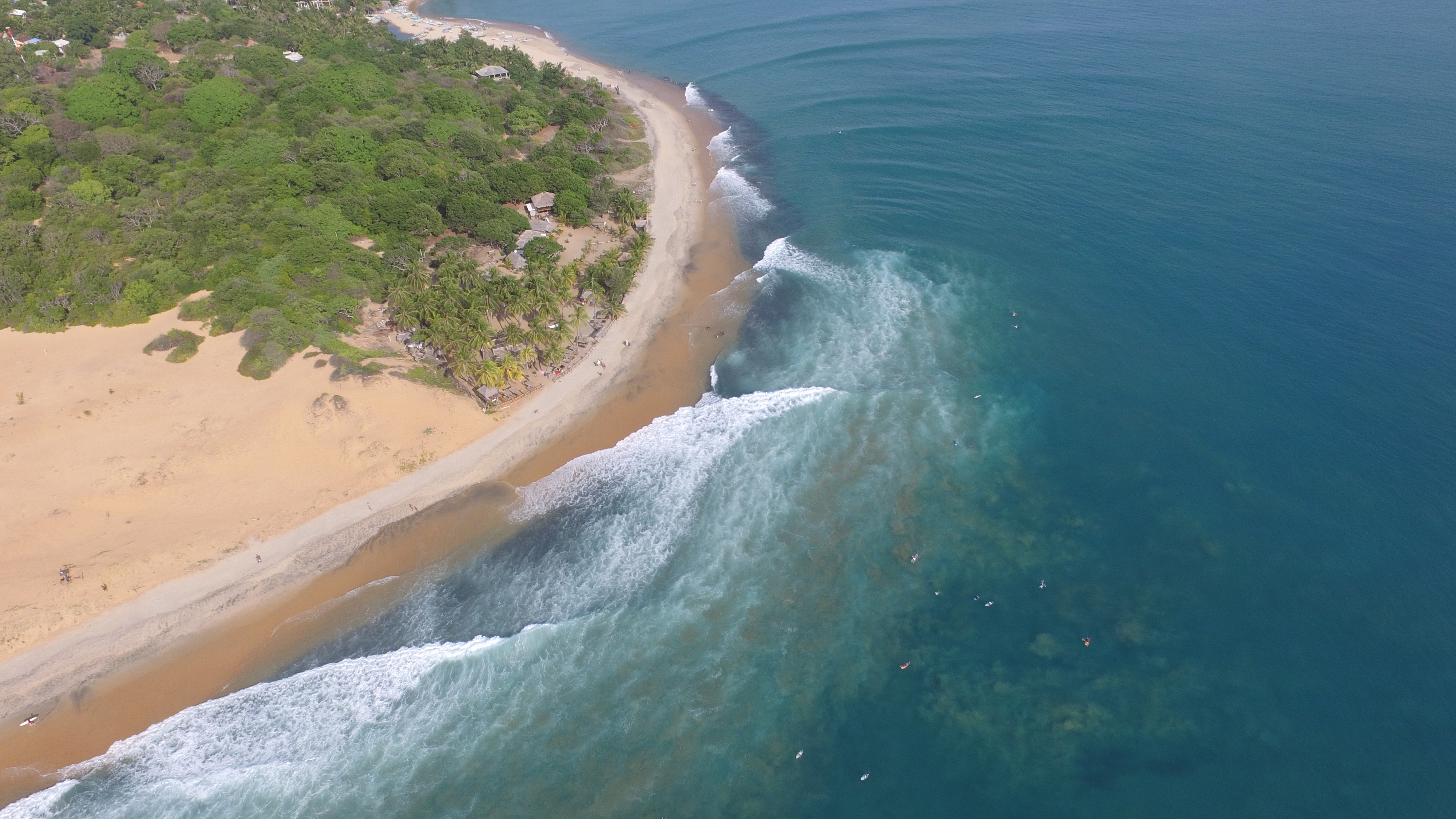 Aerial view of Main Point, Arugam Bay — the long right-hand wave wrapping the headland with surfers in the lineup