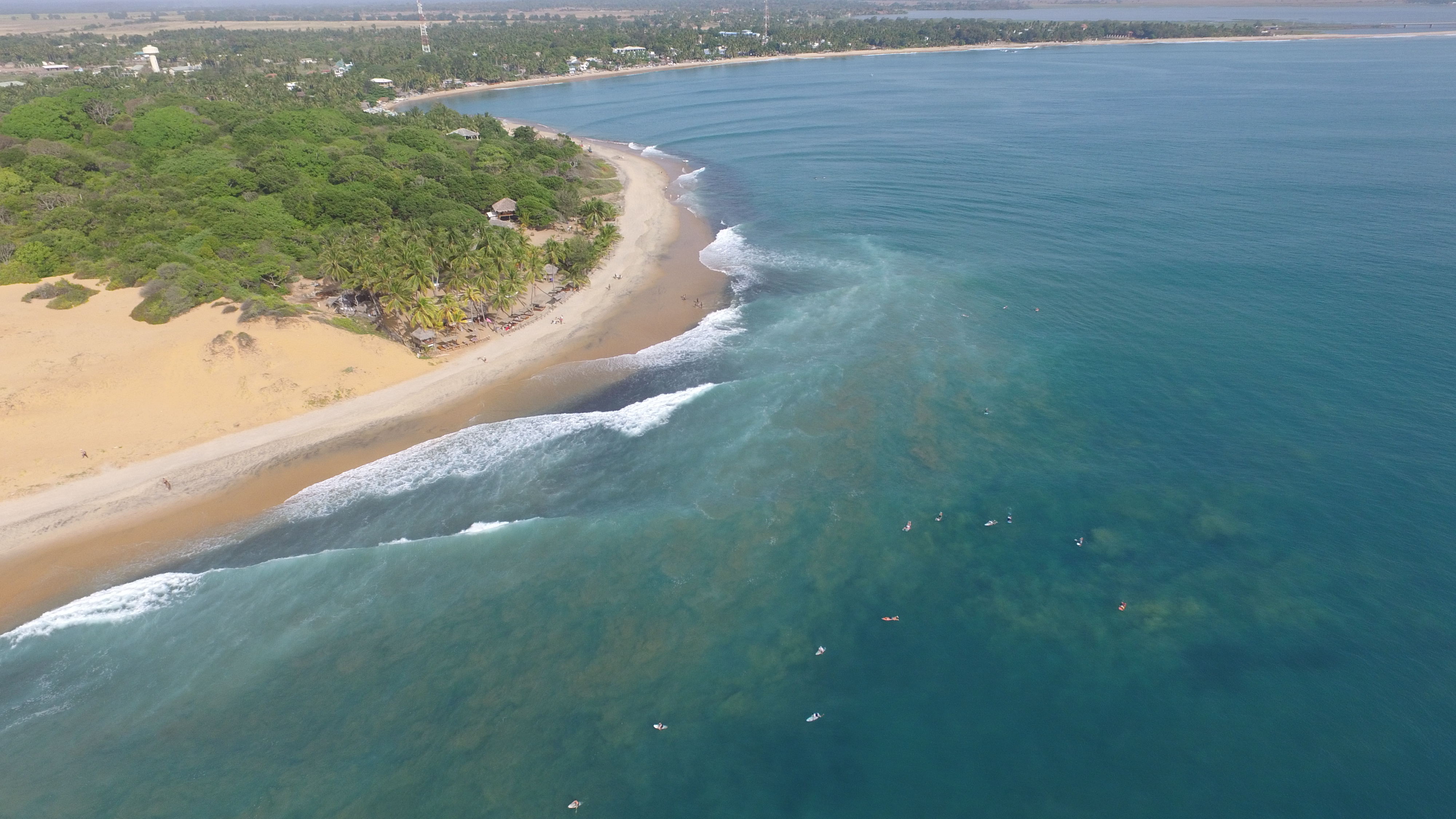 Aerial view of the headland and sweeping bay at Arugam Bay with surfers offshore