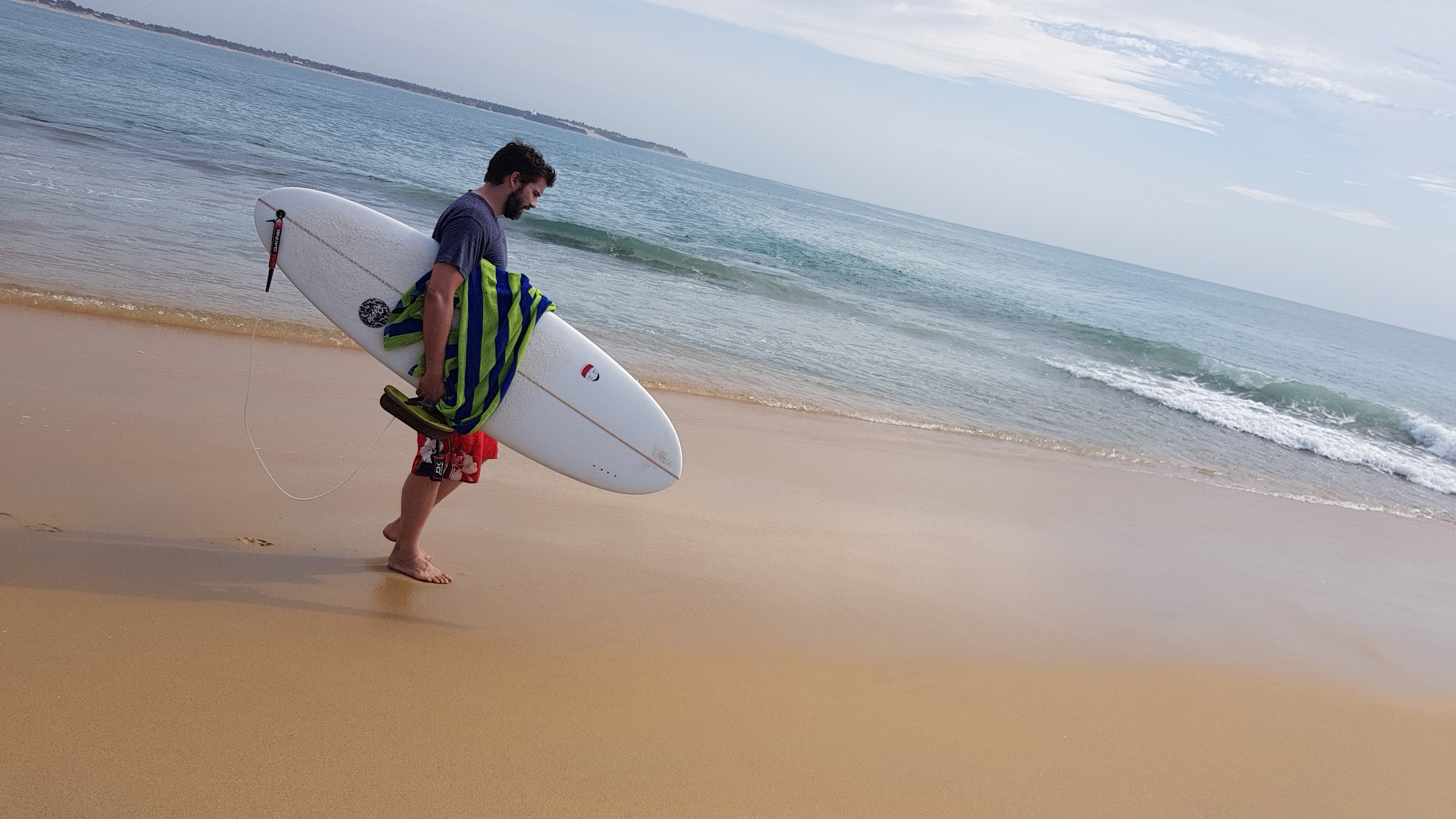A surfer carrying a board out of the water along the sand at Arugam Bay