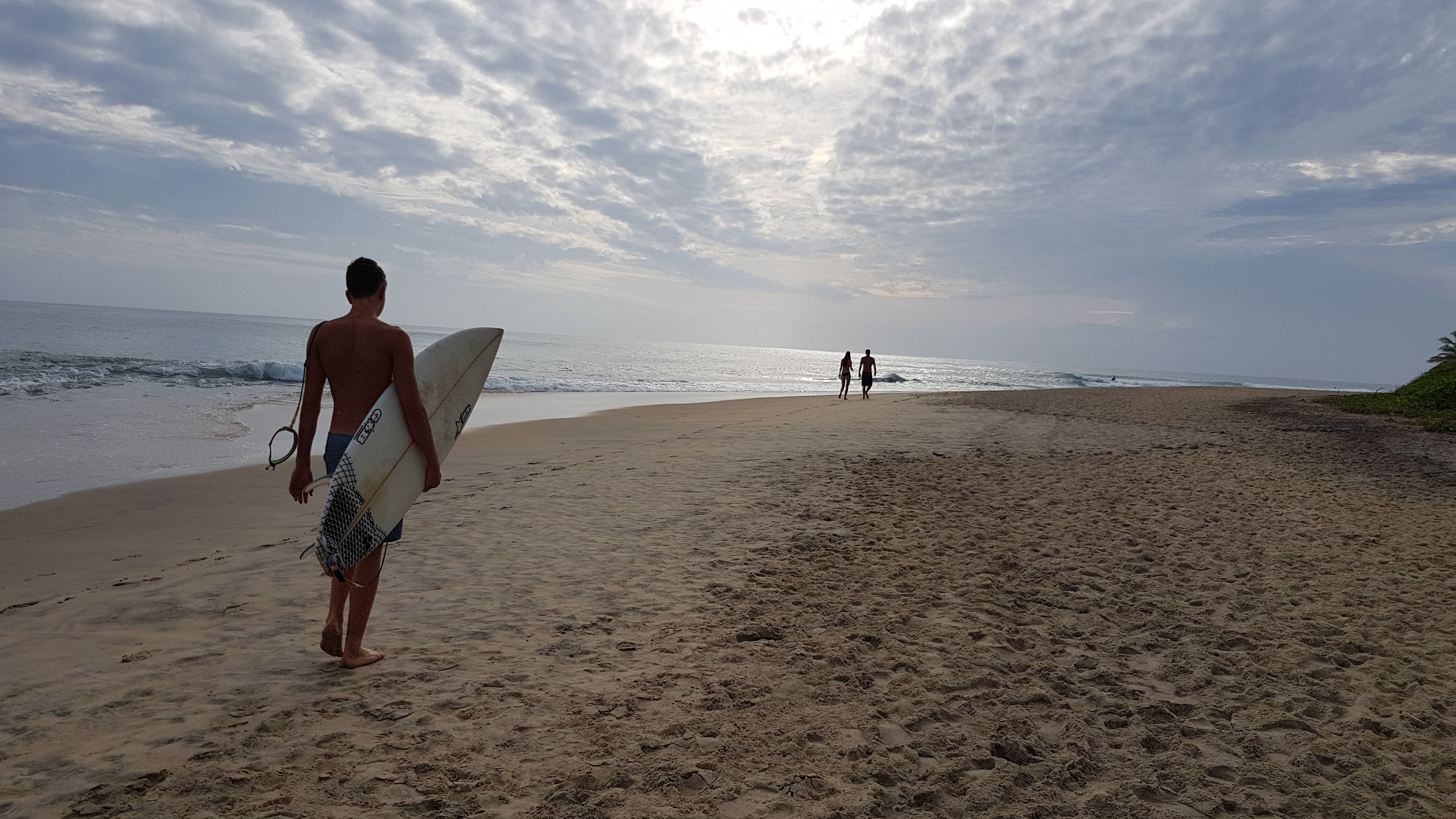 A lone surfer carrying a board along the empty beach at first light, Arugam Bay